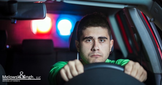 man looking concerned behind wheel of car, police lights behind him